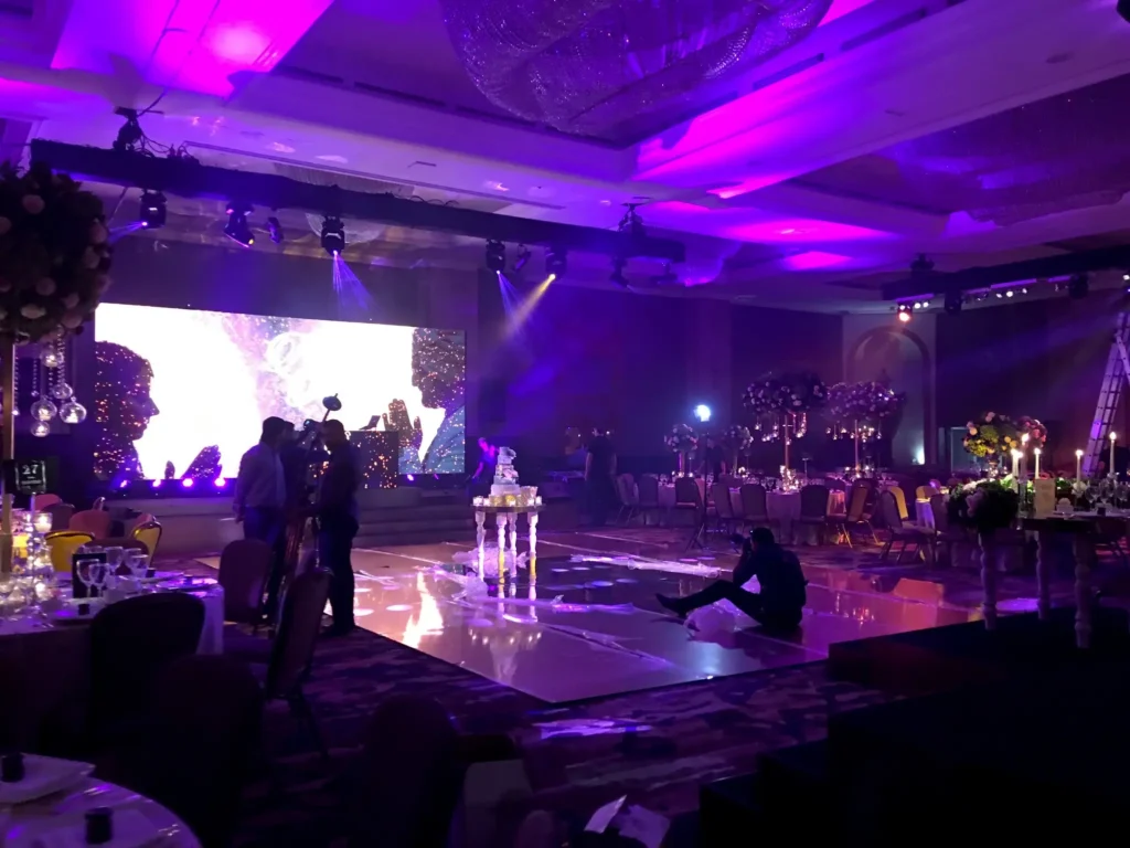 Asian wedding DJ setup with LED screen, lighting, and mirrored dance floor.
