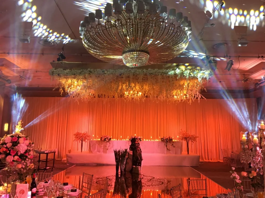 Mixed wedding reception with DJ setup, ceiling draping and warm ambient lighting.
