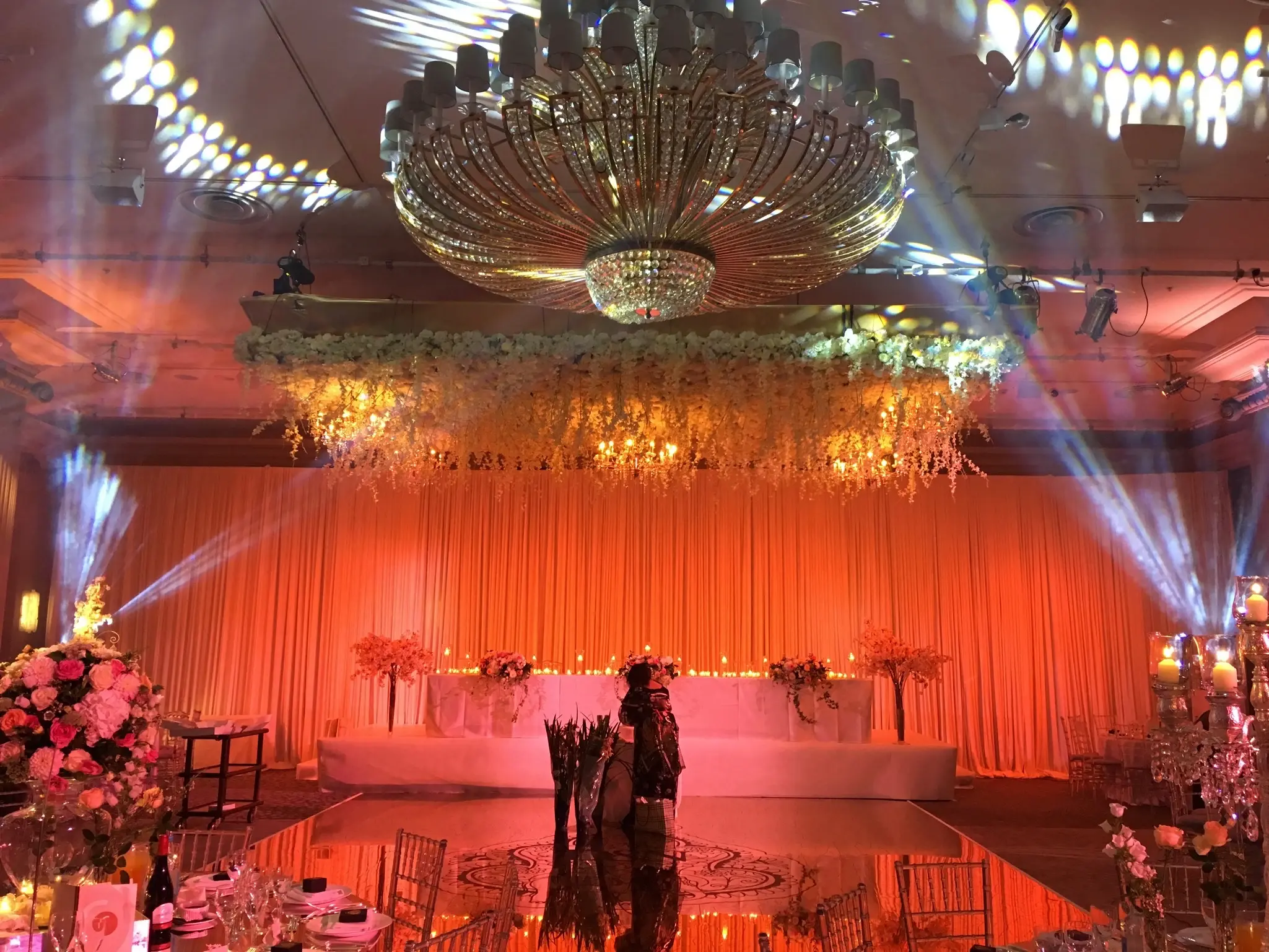 Asian wedding top table with warm event lighting, draping and floral installations.