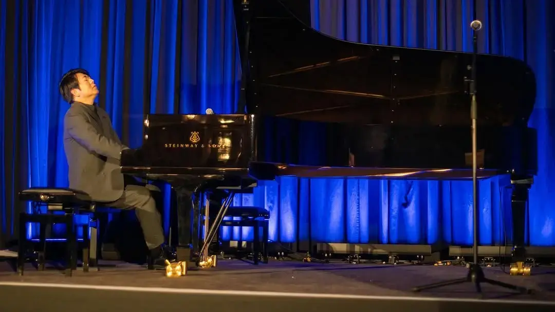 Grand piano performance on stage at charity gala dinner with professional AV lighting, microphones and event production setup.