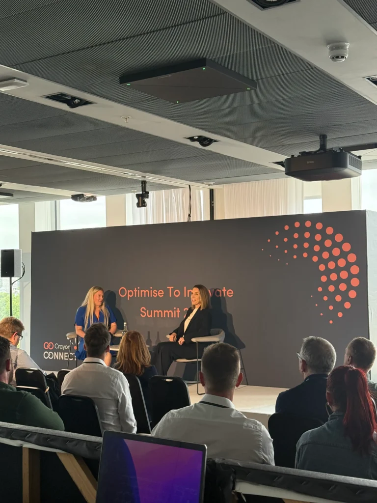 On-stage interview session at Crayon Optimise to Innovate Summit with audience seating and branded conference backdrop