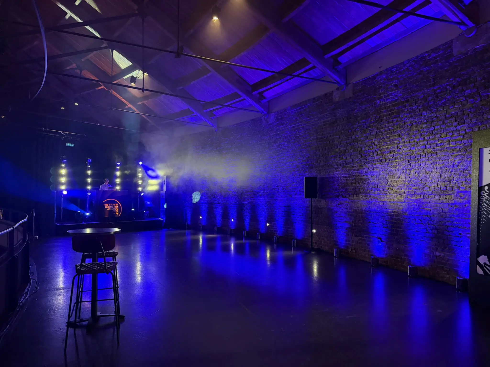 Wireless uplighting illuminating brick wall and DJ stage at corporate event production venue