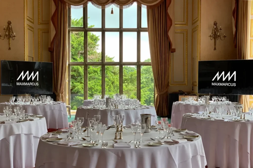 Elegant wedding reception room with two screens displaying the MaxMarcus logo
