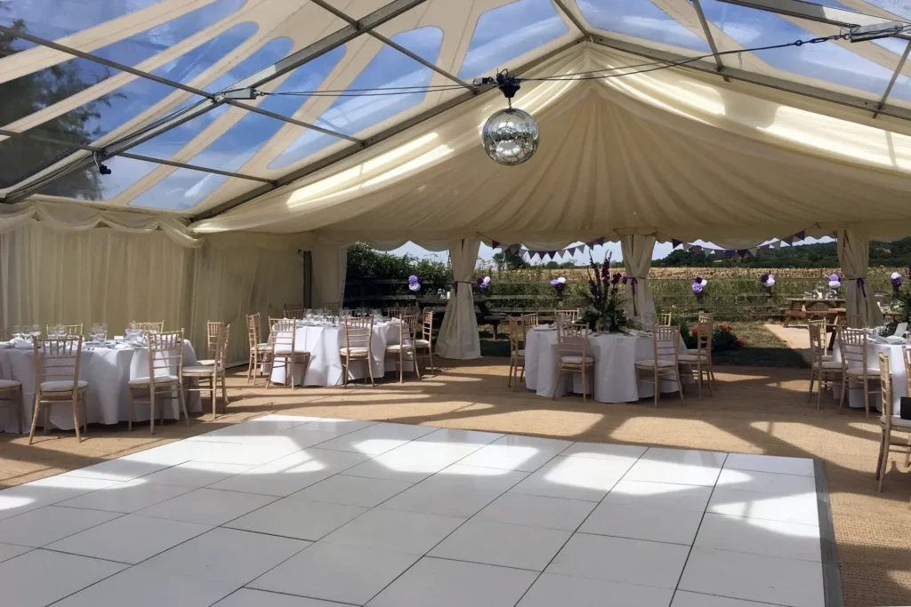 White dancefloor set inside a clear marquee wedding reception with round dining tables
