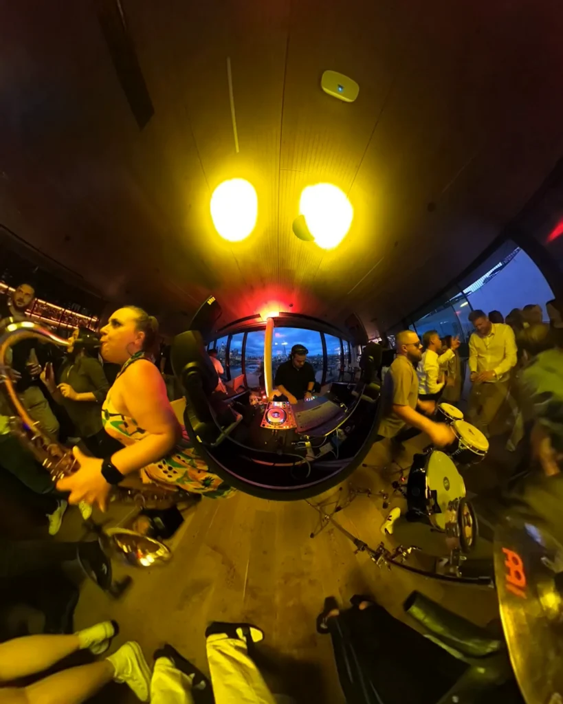 DJ with live saxophone and percussion performing at a corporate party with the London skyline behind.